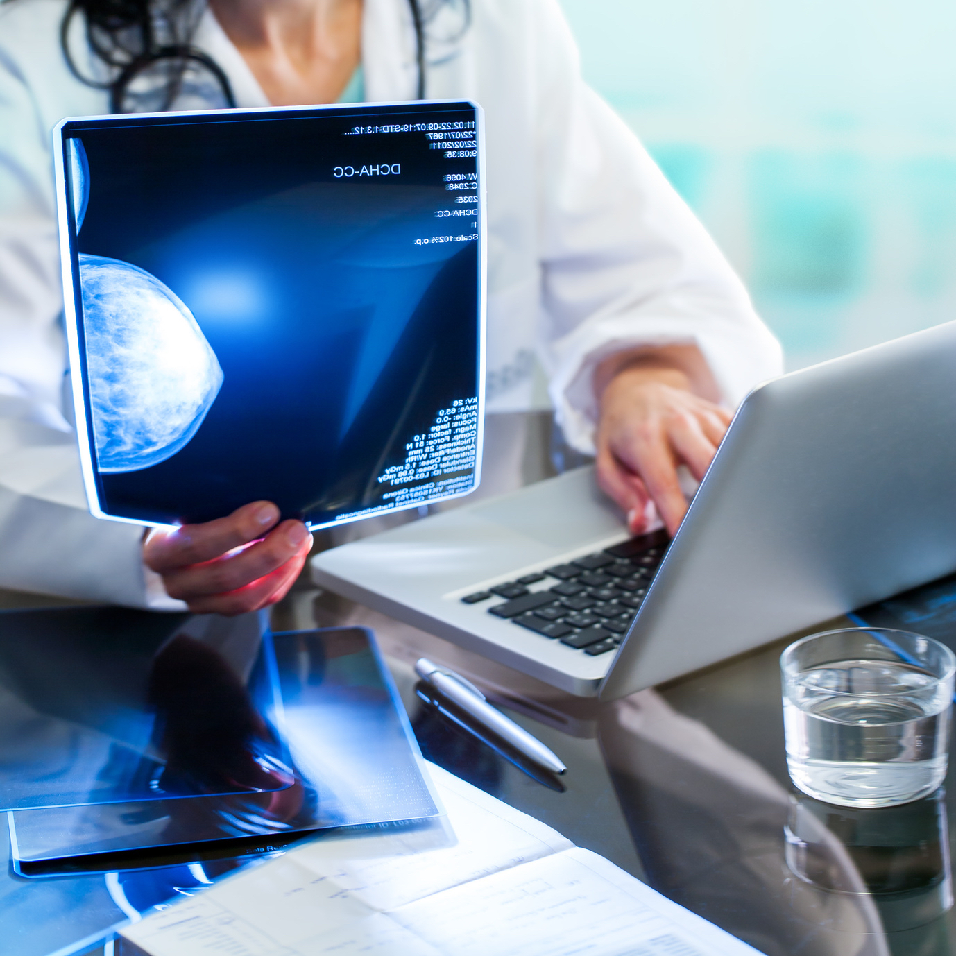 Close up of Doctor’s hands reviewing x-ray of mammogram and introducing results on laptop.